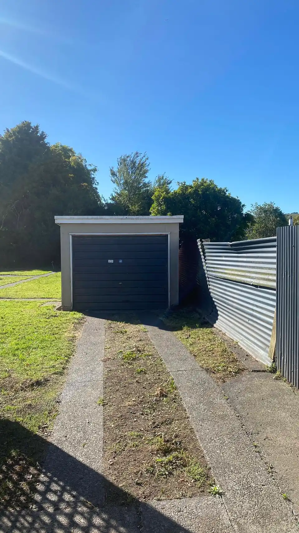 A tidy back section with mown grass either side of a concrete strip driveway running up to a garage